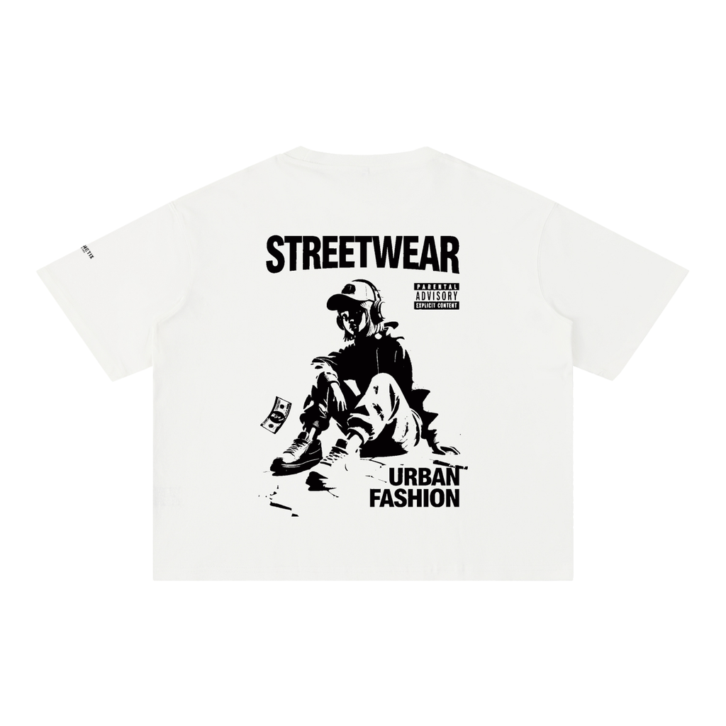 An off-white short-sleeve t-shirt with a black graphic print on the front. The graphic features the text 'STREETWEAR' and 'URBAN FASHION' surrounding a stylized illustration of a person sitting on the ground with a skateboard.