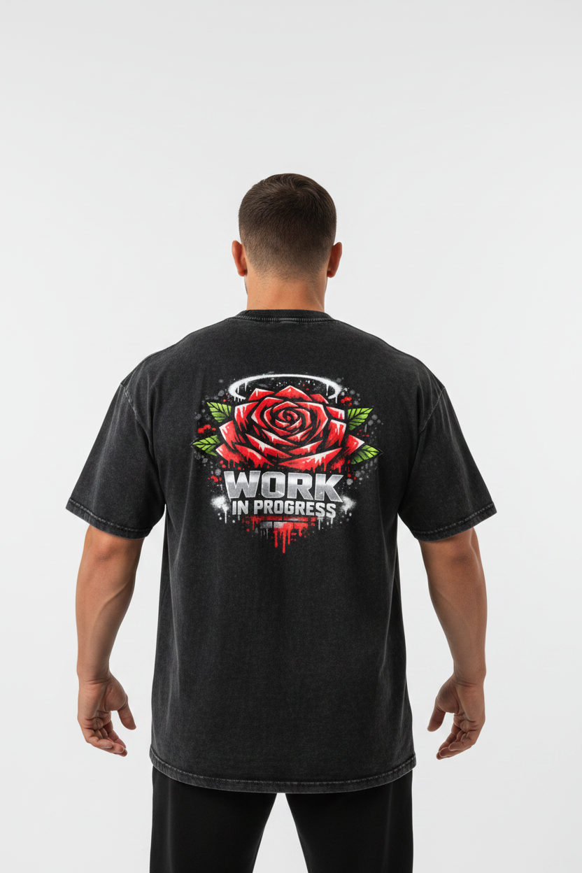 A black acid-wash t-shirt shown from the back, featuring a graphic of a red rose with green leaves and the text 'WORK IN PROGRESS' in white and red.